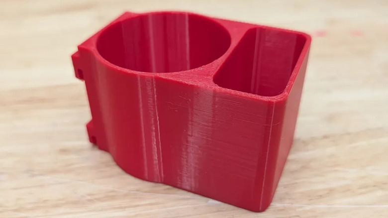 Клеевой держатель, напечатанный на 3D-принтере, для красного стеллажа Home Depot, опирающийся на деревянную поверхность.