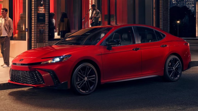 Красная Toyota Camry припаркована ночью на улице города.