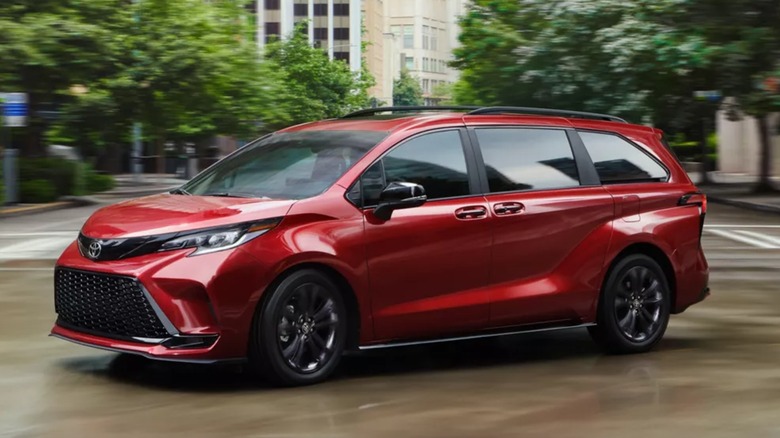 Красная Toyota Sienna движется по городскому перекрестку.