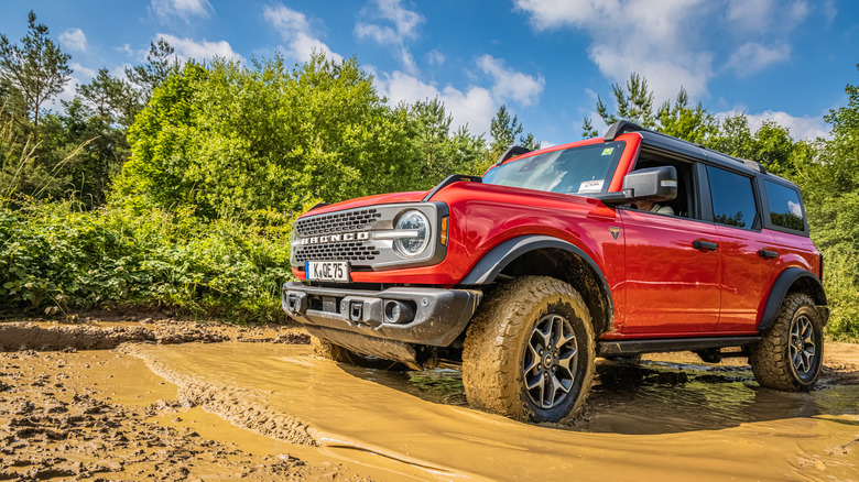 Красный Ford Bronco проезжает по очень грязной луже.