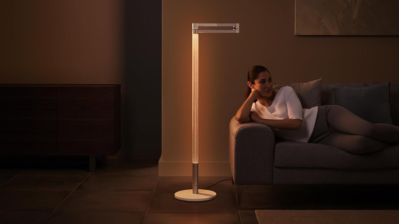 Человек, развалившийся на диване рядом с торшером Dyson Solarcycle Morph.