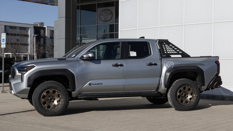 Вид сбоку серебристой Toyota Tacoma Trailhunter, припаркованной перед дилерским центром Toyota.
