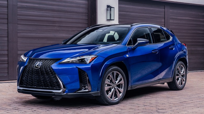 Вид спереди на 3/4 Lexus UX300h 2026 года выпуска на кирпичной поверхности перед гаражами