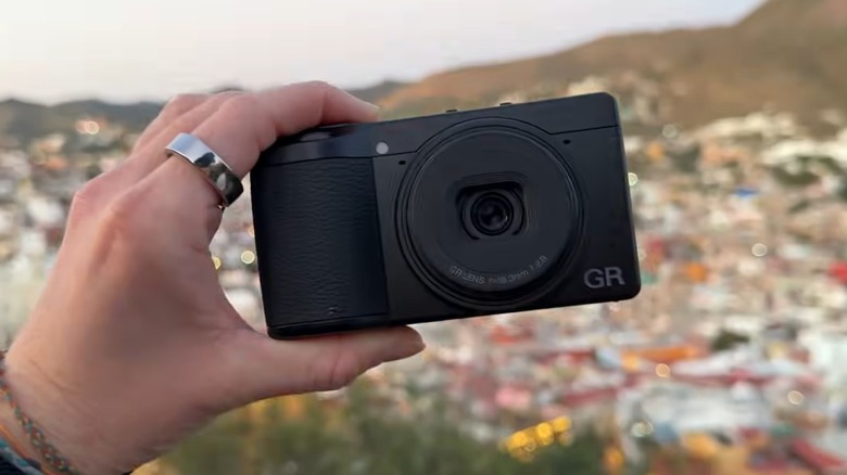 Человек снаружи держит камеру Ricoh GR IV.