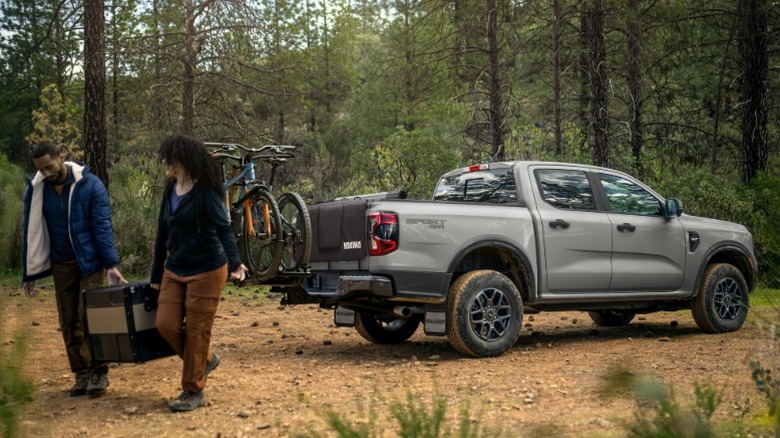 Два человека выгружают походное снаряжение из серого Ford Ranger в лесу