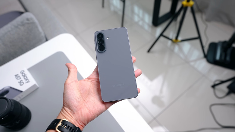 Человек держит Samsung Galaxy A57 5G серого цвета.
