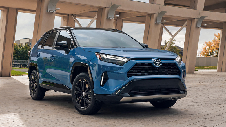 Синий Toyota RAV4 Hybrid 2025 года выпуска, вид спереди в 3/4, на заднем плане современная конструкция