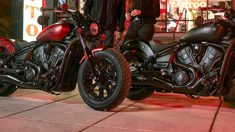 Два мотоцикла Indian Scout 2026 года выпуска — красный и черный — припаркованы бок о бок перед кафе ночью.