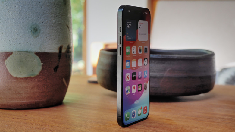 iPhone 15 Pro Max стоит вертикально на столе с керамикой на заднем плане