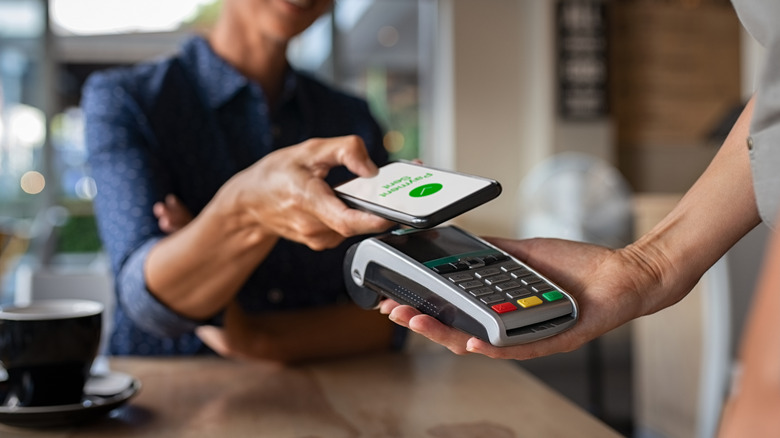 Человек оплачивает счет через смартфон с использованием технологии NFC