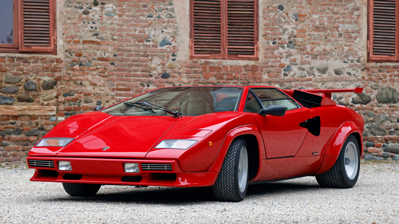 На снимке изображен Lamborghini Countach, припаркованный на гравийной стоянке.