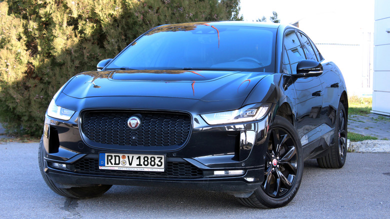 Черный электромобиль Jaguar I-Pace EV припаркован перед кустами и зданием.