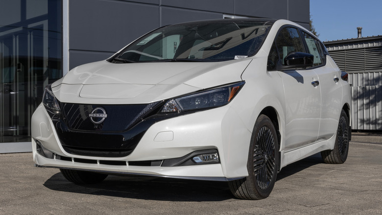 Новый белый Nissan LEAF EV припаркован перед автосалоном.