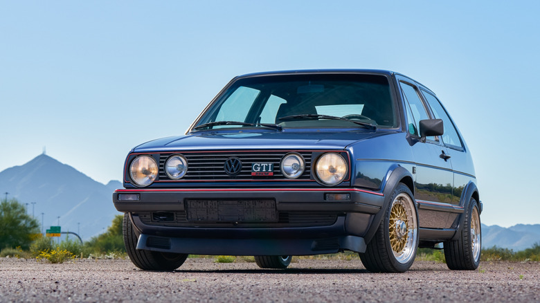 Вид спереди в 3/4 на Volkswagen Golf Mk2 GTI 1987 года выпуска, припаркованный перед горами.