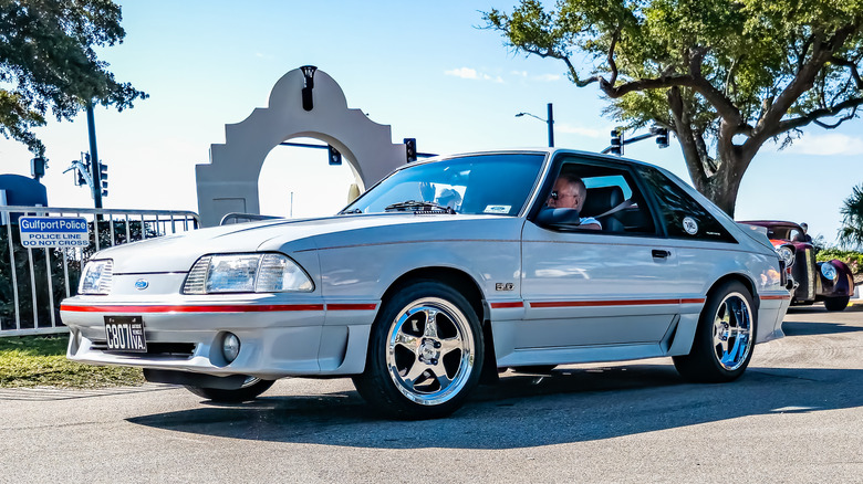 Вид спереди 3/4 на белый и красный Fox Body Ford Mustang GT на автосалоне.