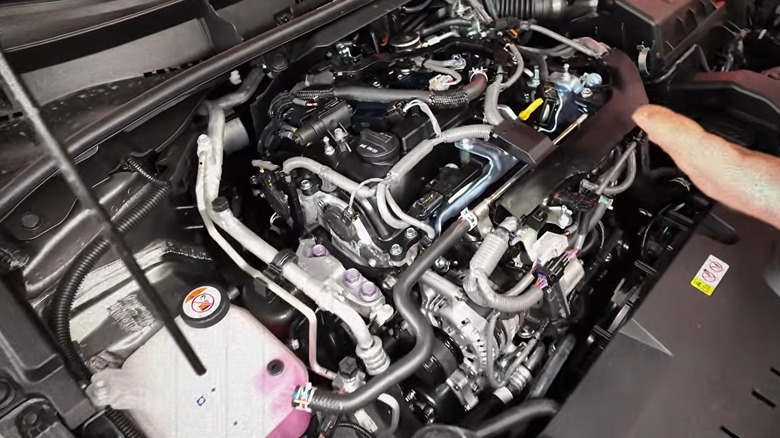 Плотно упакованный моторный отсек Toyota G16E-GTS с открытым трехцилиндровым агрегатом, окруженным паутиной шлангов, проводки и водопровода.