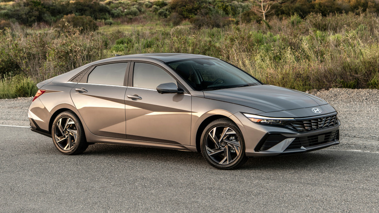 Вид спереди в 3/4 на серый Hyundai Elantra 2026 года выпуска, припаркованный перед высокой травой