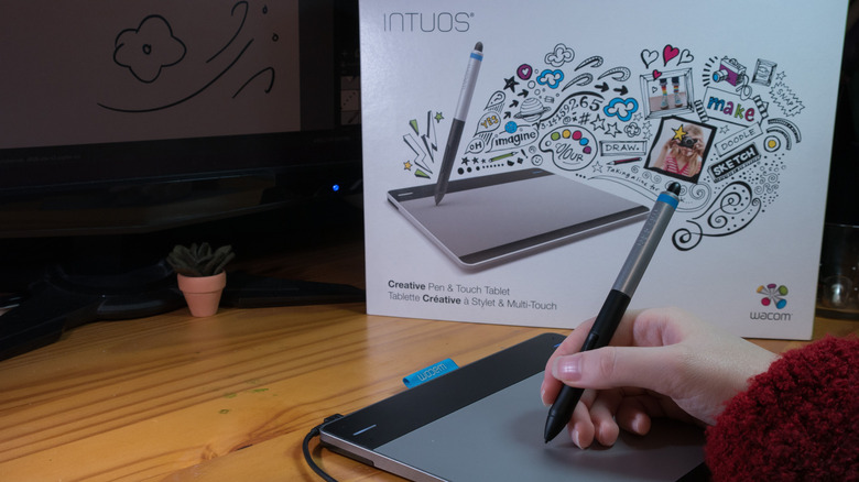 Рука использует стилус на планшете Wacom Intuos, блок Intuos на заднем плане.