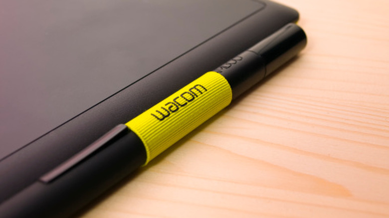 Стилус Wacom на деревянном столе рядом с планшетом.