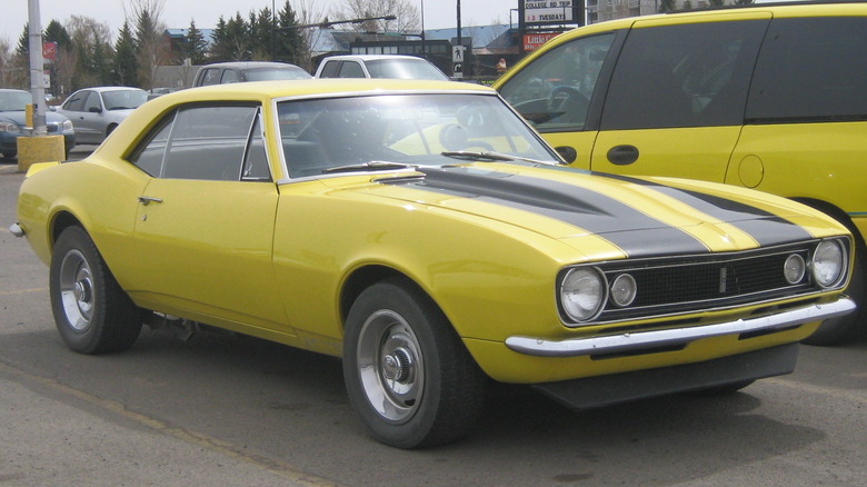 Chevrolet Camaro 1967 года желтого цвета с черными гоночными полосами стоит на парковке