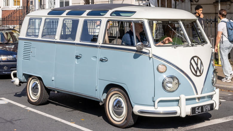 Volkswagen Van 1964 года в бело-голубом цвете, стоит на холостом ходу у пешеходного перехода.