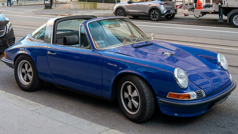 Синий кабриолет Porsche 911, припаркованный у тротуара.