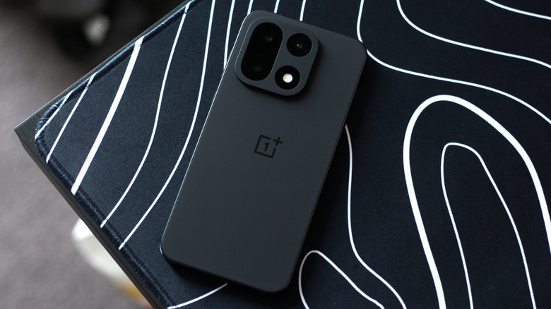 Черный OnePlus 15 на коврике для мыши с абстрактным бело-черным узором.