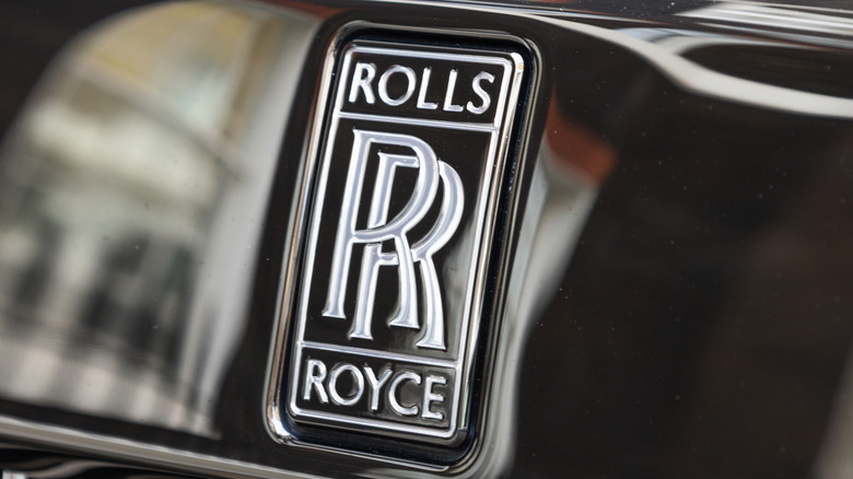 Крупный план серебристого логотипа Rolls-Royce на черном автомобиле.
