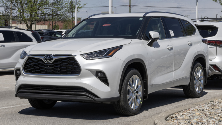 Вид спереди на 3/4 белой Toyota Highlander, припаркованной на стоянке дилера Toyota.
