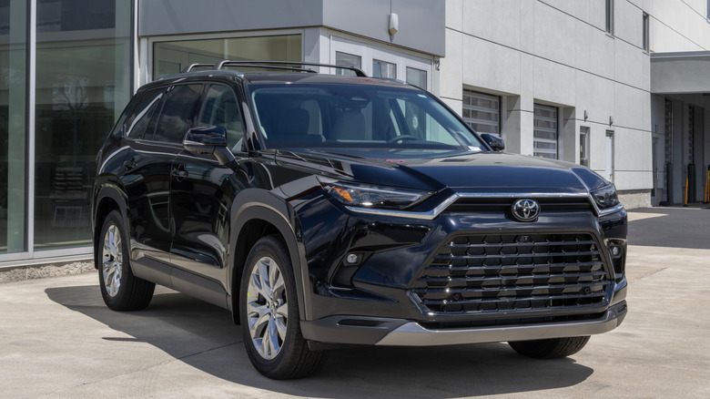 Вид спереди в 3/4 на черную Toyota Grand Highlander, припаркованную перед дилерским центром Toyota.