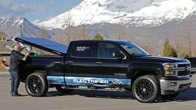 Вид человека, поднимающего солнечную крышку тонно на черном пикапе Chevy Silverado.