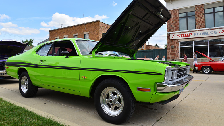 Вид спереди на 3/4 зеленого Dodge Demon 1970-х годов, припаркованного на автосалоне.
