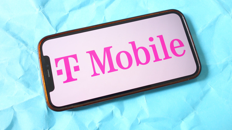 Изображение смартфона с розовым логотипом T-Mobile на синем фоне.