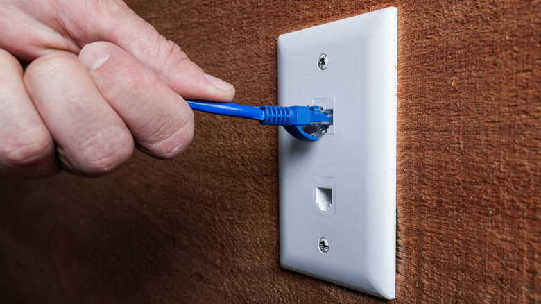 Крупный план руки, подключающей кабель Ethernet к настенной розетке RJ45.