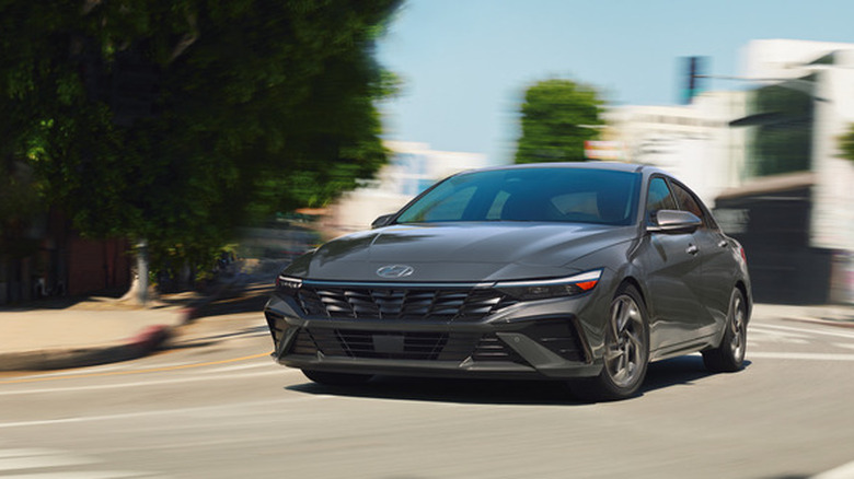 Вид спереди на серый Hyundai Elantra Hybrid, едущий по городской улице.