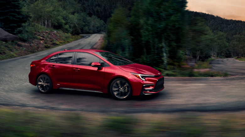 Вид сбоку на красную Toyota Corolla Hybrid, едущую по горной дороге.