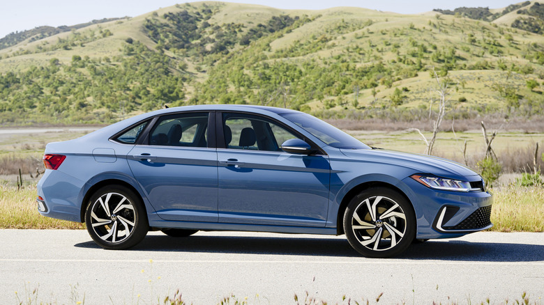 Вид сбоку на серый седан Volkswagen Jetta, припаркованный перед предгорьями.