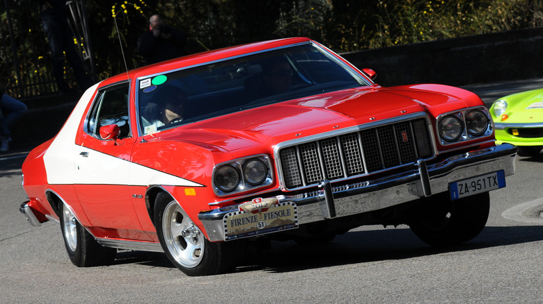 Вид спереди на точную копию Ford Torino компании Starsky & Hutch, поворачивающую за угол во время ралли классических автомобилей.