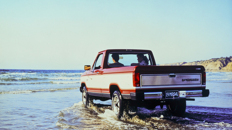 1985 год. База Ford Ranger Base проезжает по мелководью по приливному пляжу, вид сзади слева в 3/4.