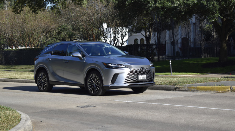 Серебристый Lexus RX 2026 года едет по небольшой дороге.
