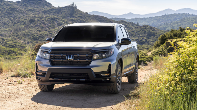 Серебристая Honda Ridgeline 2026 года выпуска на грунтовой дороге, на заднем плане горы.