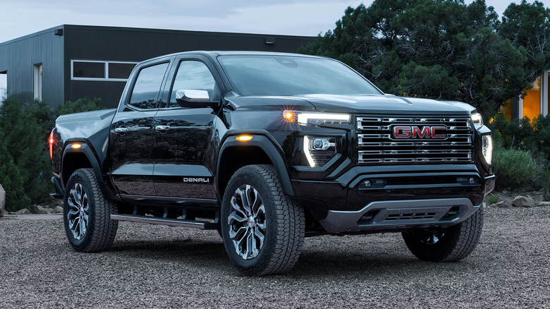 Черный GMC Canyon 2026 года выпуска припаркован на пригородной гравийной парковке.