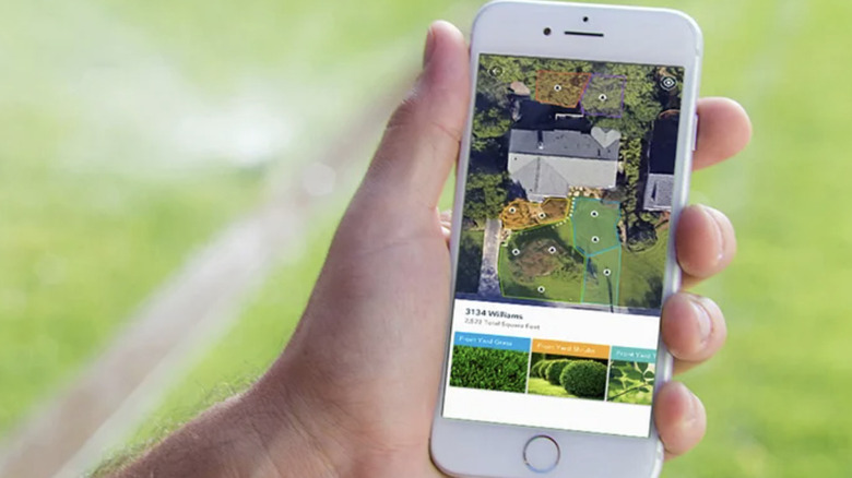 Крупный план руки, держащей смартфон, на котором отображается приложение Rachio Smart Sprinkler System.