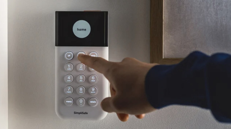 Крупный план руки, тянущейся к клавиатуре системы безопасности SimpliSafe.