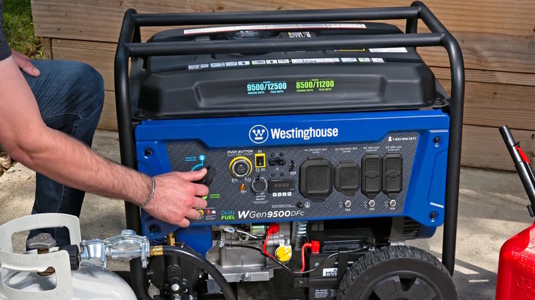 Человек включает портативный генератор рядом с баллонами с бензином и пропаном