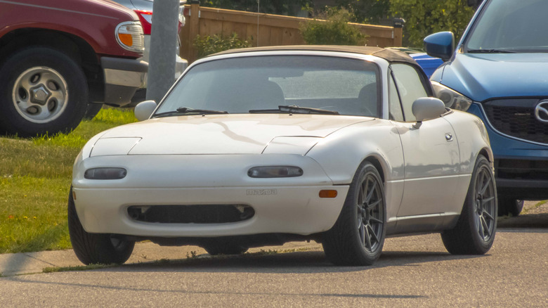 Вид спереди белой Mazda Miata, припаркованной на улице.