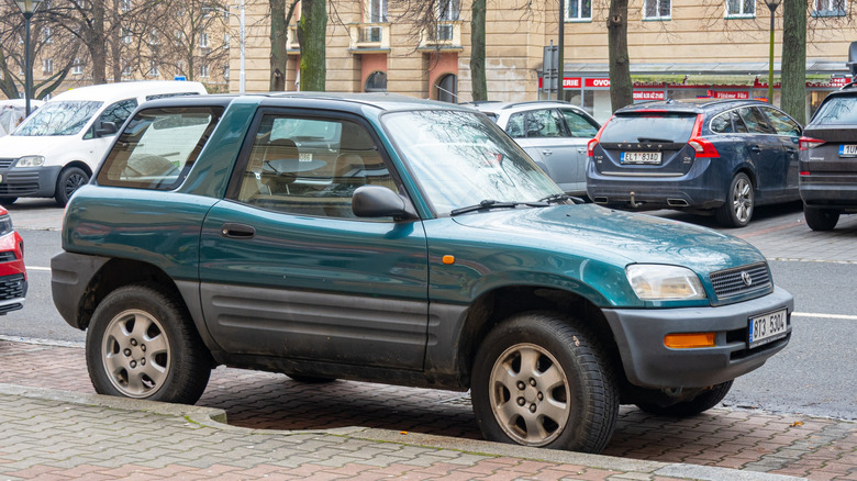 Вид сбоку на зеленую Toyota RAV4 первого поколения, припаркованную на городской улице.