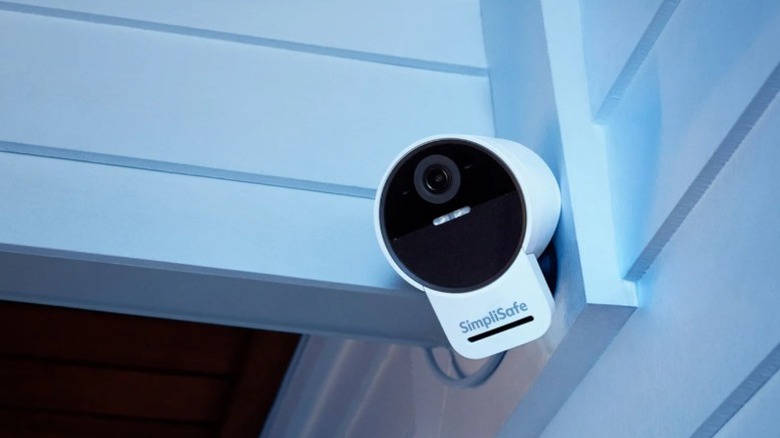 Камера наружного наблюдения SimpliSafe, установленная на белом сайдинге.