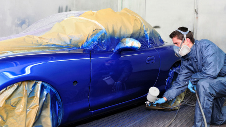 Автотехник распыляет Mazda MX-5 синей краской в ​​профессиональной покрасочной камере