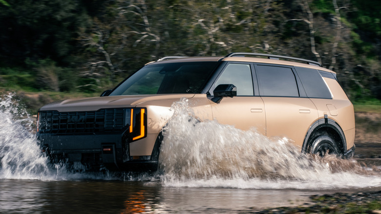 Вид спереди на 3/4: Kia Telluride пересекает ручей в лесу.
